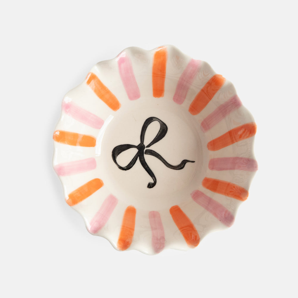 scalloped edge glazed stoneware cereal bowl with pink and orange stripes and black bow design inside