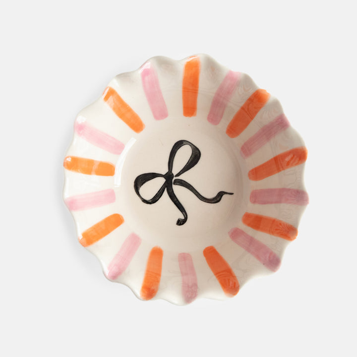 scalloped edge glazed stoneware cereal bowl with pink and orange stripes and black bow design inside