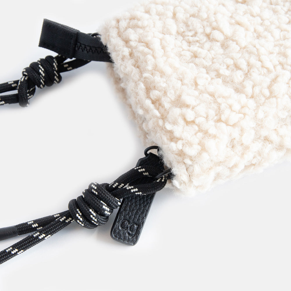 synthetic cream borg phone bag with a monochrome adjustable cord strap and black zip pull