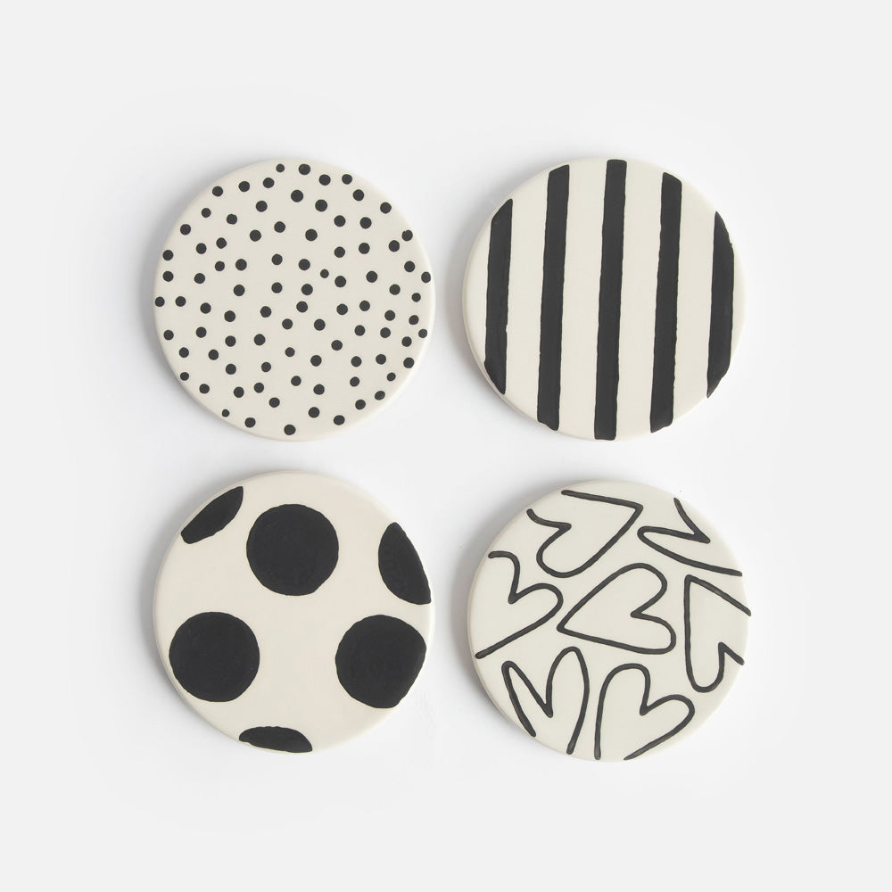 set of four round hand painted ceramic stoneware coasters with black spots, stripes and hearts designs and anti slip silicone feet