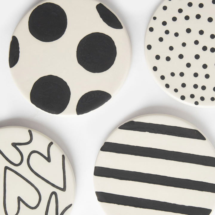 set of four round hand painted ceramic stoneware coasters with black spots, stripes and hearts designs and anti slip silicone feet