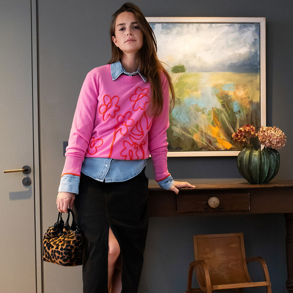 woman wearing a pink jumper with red floral stitch design over a light denim shirt