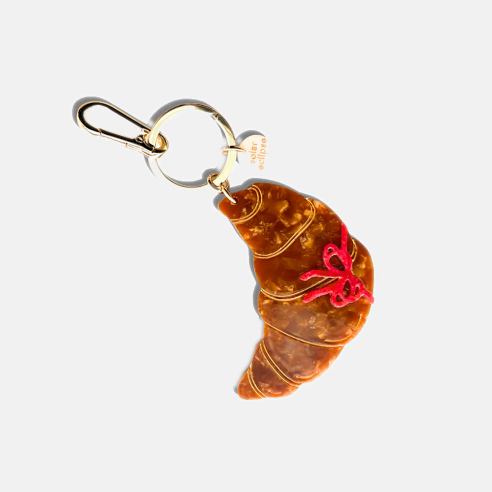 A hand-painted croissant-shaped bag charm with a red flower detail and a metallic clasp for attachment.