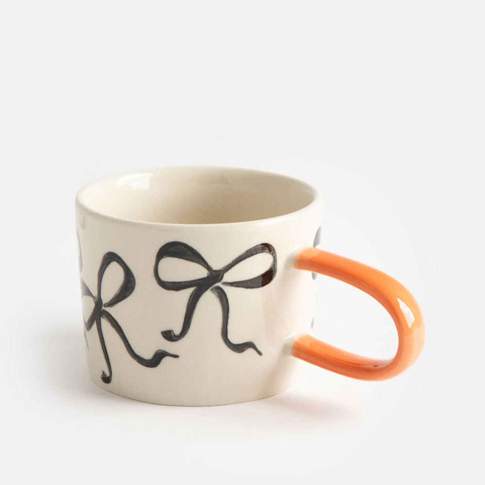 hand painted ceramic stoneware mug with black bows design and an orange elongated handle
