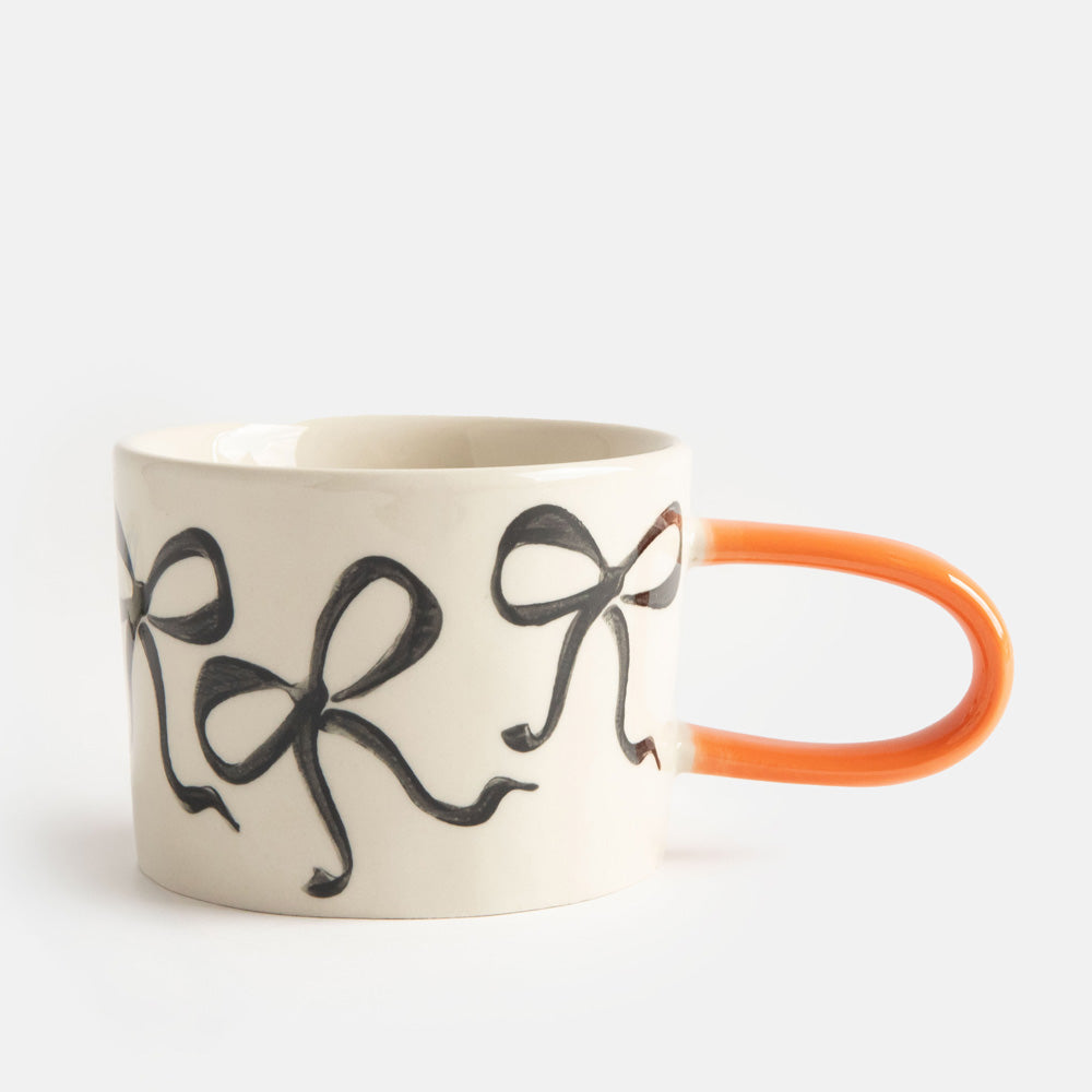hand painted ceramic stoneware mug with black bows design and an orange elongated handle