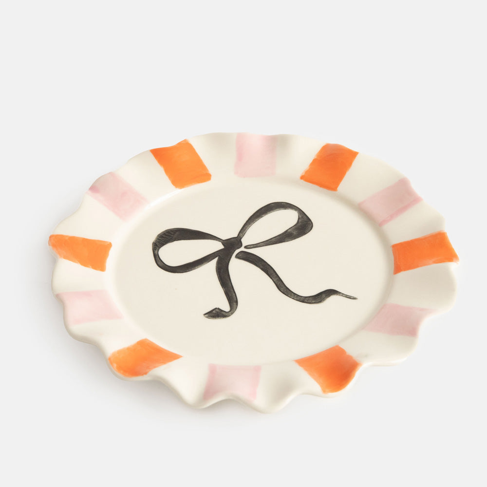 hand painted ceramic stoneware plate with soft pink and orange stripe scalloped edge and black bow design on the centre