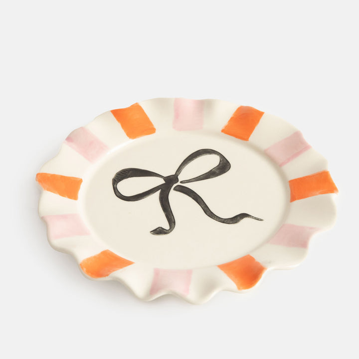 hand painted ceramic stoneware plate with soft pink and orange stripe scalloped edge and black bow design on the centre