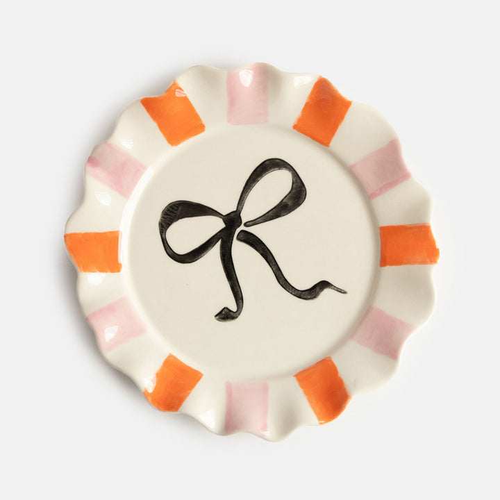 hand painted ceramic stoneware plate with soft pink and orange stripe scalloped edge and black bow design on the centre