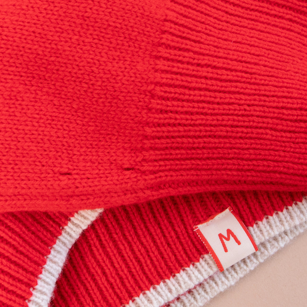 Close-up of a red knit garment with a size label 'M' on a beige background