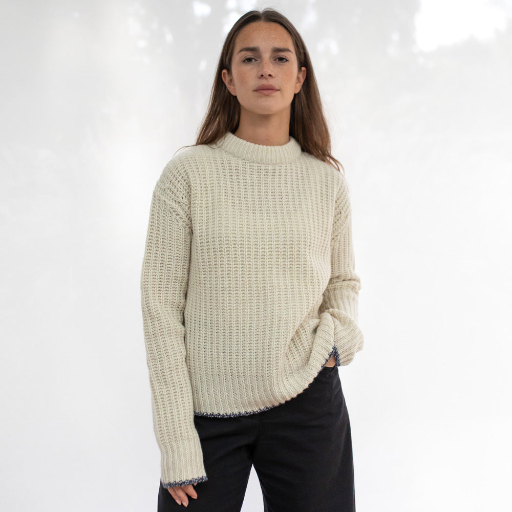Woman wearing a cream knitted sweater against a white background