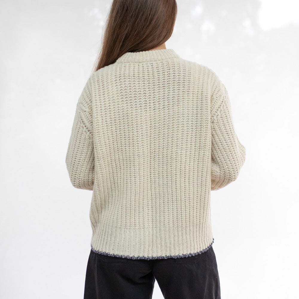 Person wearing a beige knitted sweater on a white background