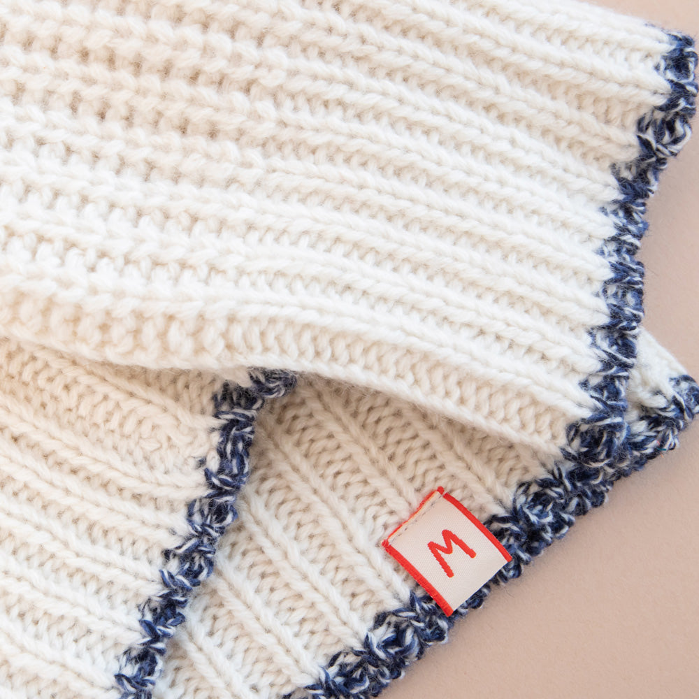 Knitted jumper with blue trim and a brand label on a beige background