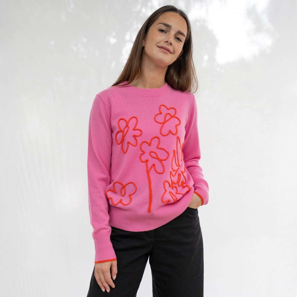 Person wearing a pink sweater with orange floral patterns on a white background