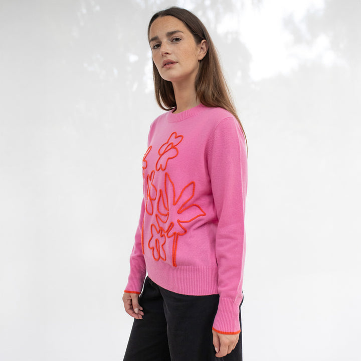 Woman wearing a pink sweater with orange floral designs on a white background