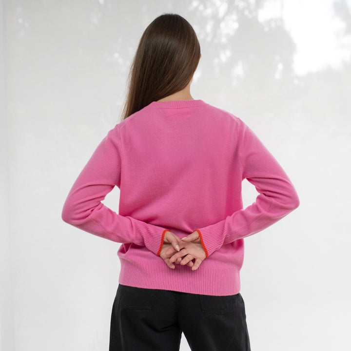 Person wearing a pink sweater with black pants on a white background