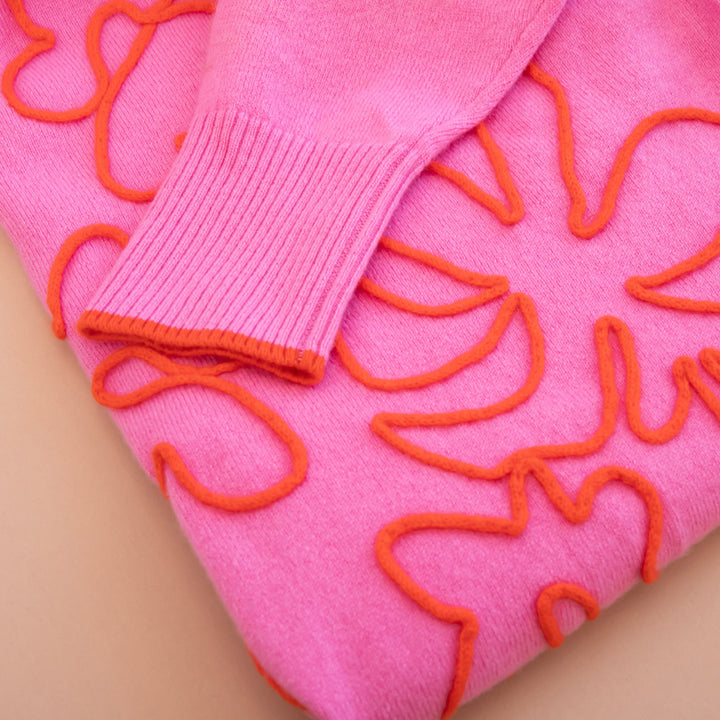 Pink sweater with orange floral patterns on a beige background