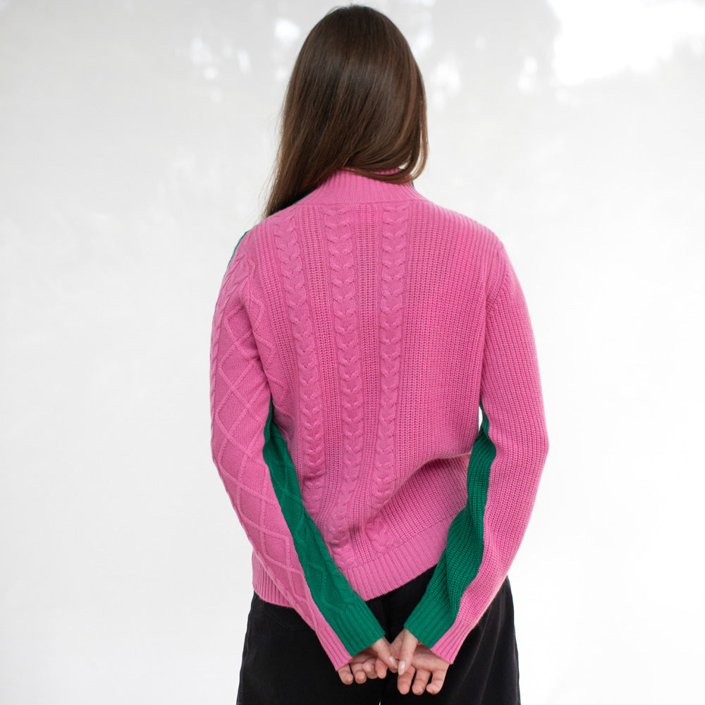 Person wearing a pink sweater with green accents on a white background