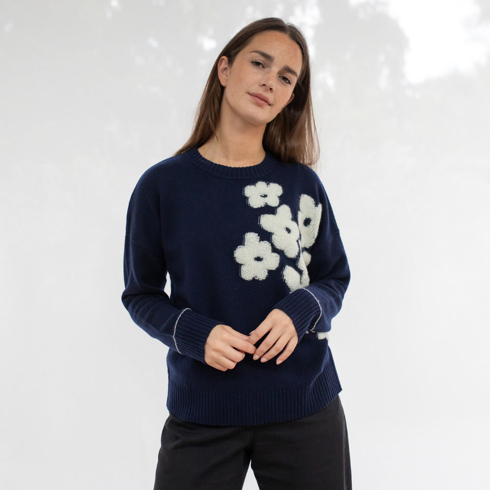 Woman wearing a navy sweater with white floral patterns on a light gray background