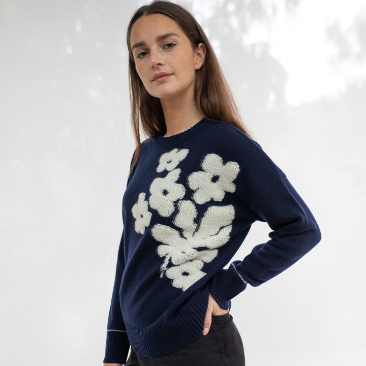 Woman wearing a navy blue sweater with white floral patterns on a light gray background