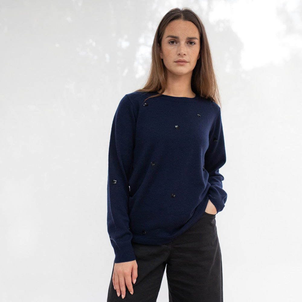 Woman wearing a navy blue sweater with small decorative buttons on a white background