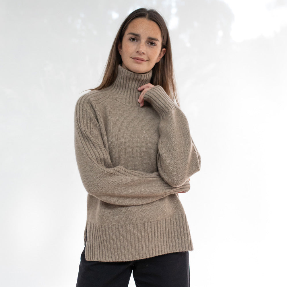 Woman wearing a beige turtleneck sweater on a white background