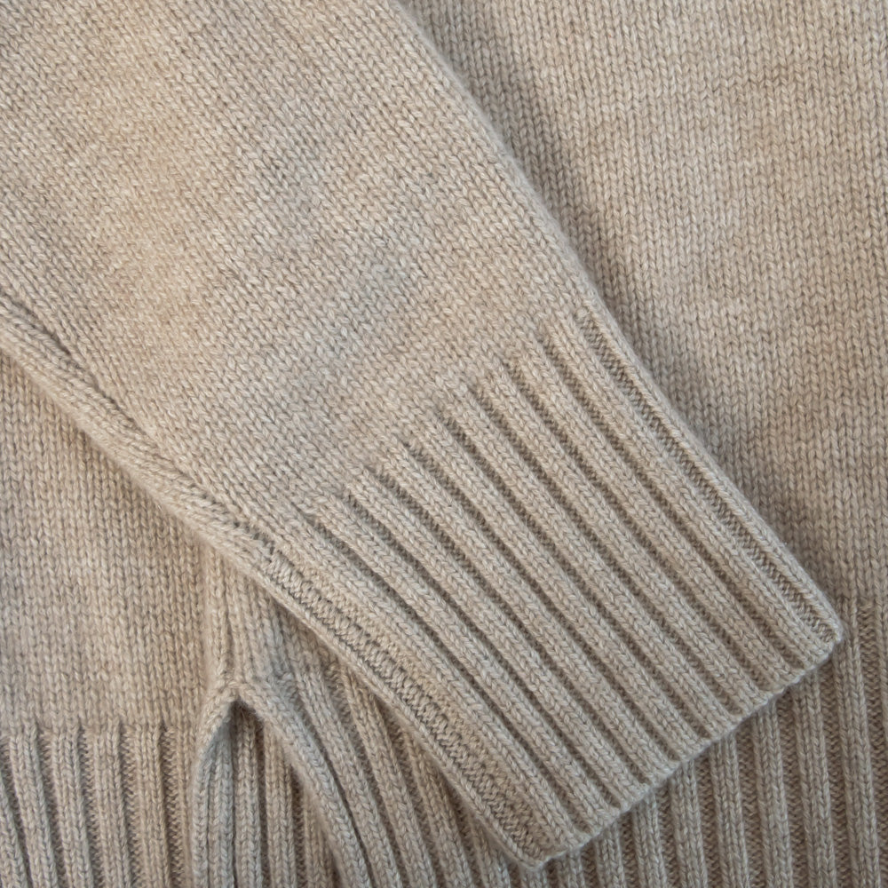 Close-up of a beige knitted sweater with ribbed cuffs and hem.