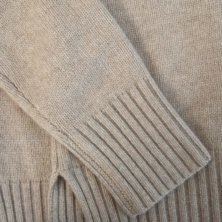 Close-up of a beige knitted sweater with ribbed cuffs and hem.