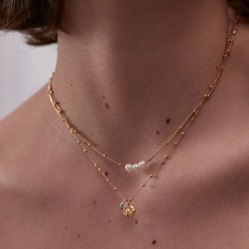 fine gold chain & bead necklace with two hammered pebble charms, one larger gold pebble and one smaller silver pebble