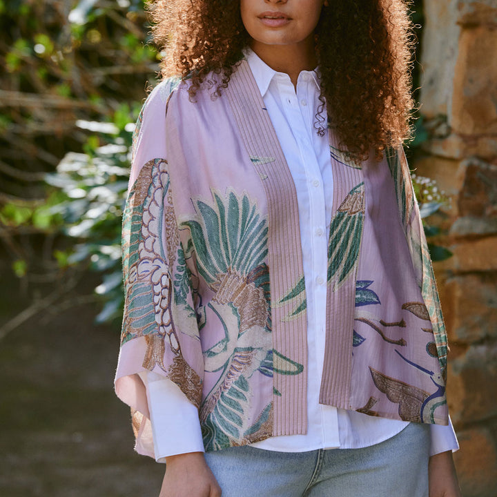 women's short kimono top featuring a design of cranes in green, brown & blue on a pale pink base