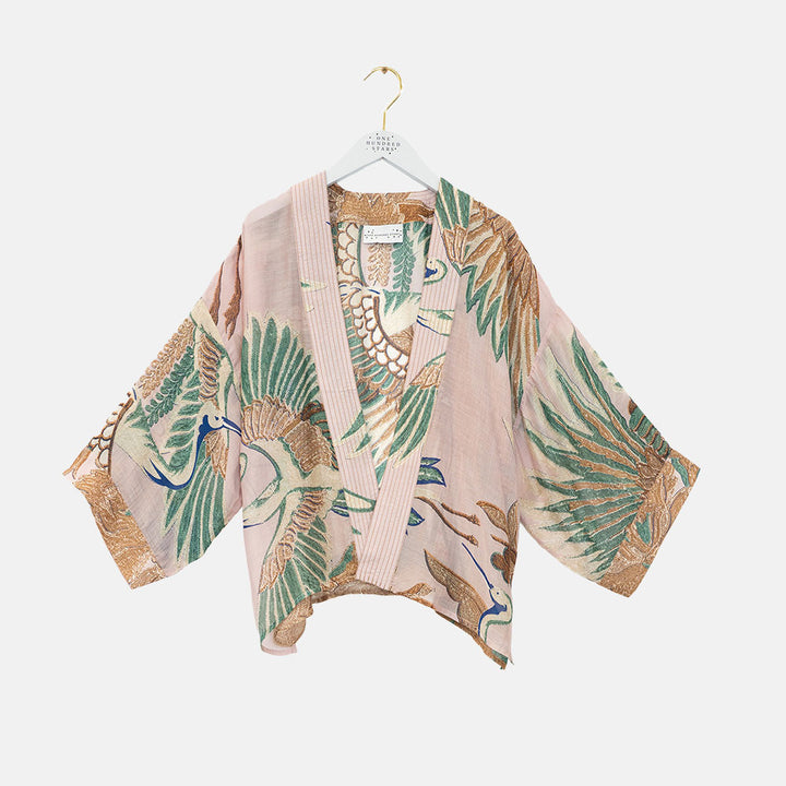 women's short kimono top featuring a design of cranes in green, brown & blue on a pale pink base