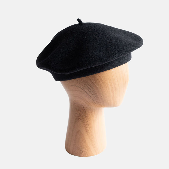 Black beret on a wooden mannequin head against a white background