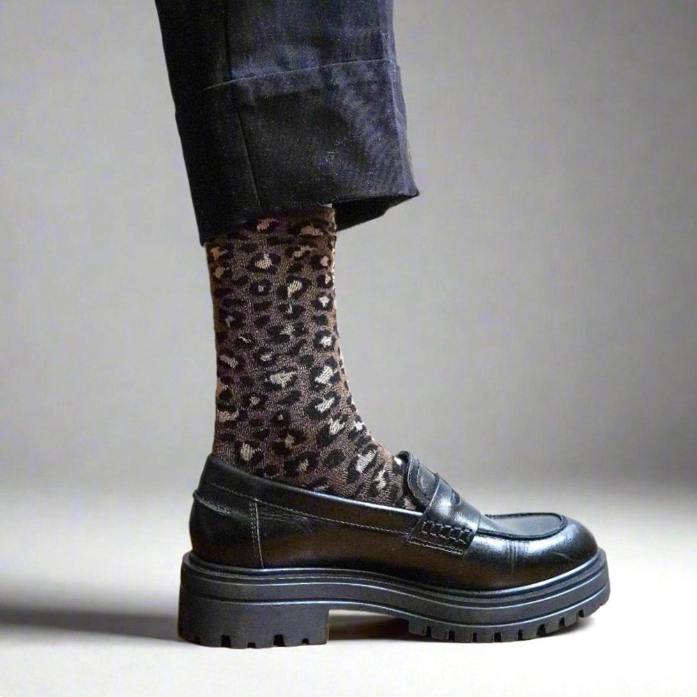 Person wearing brown leopard print socks with a black shoe on a neutral background
