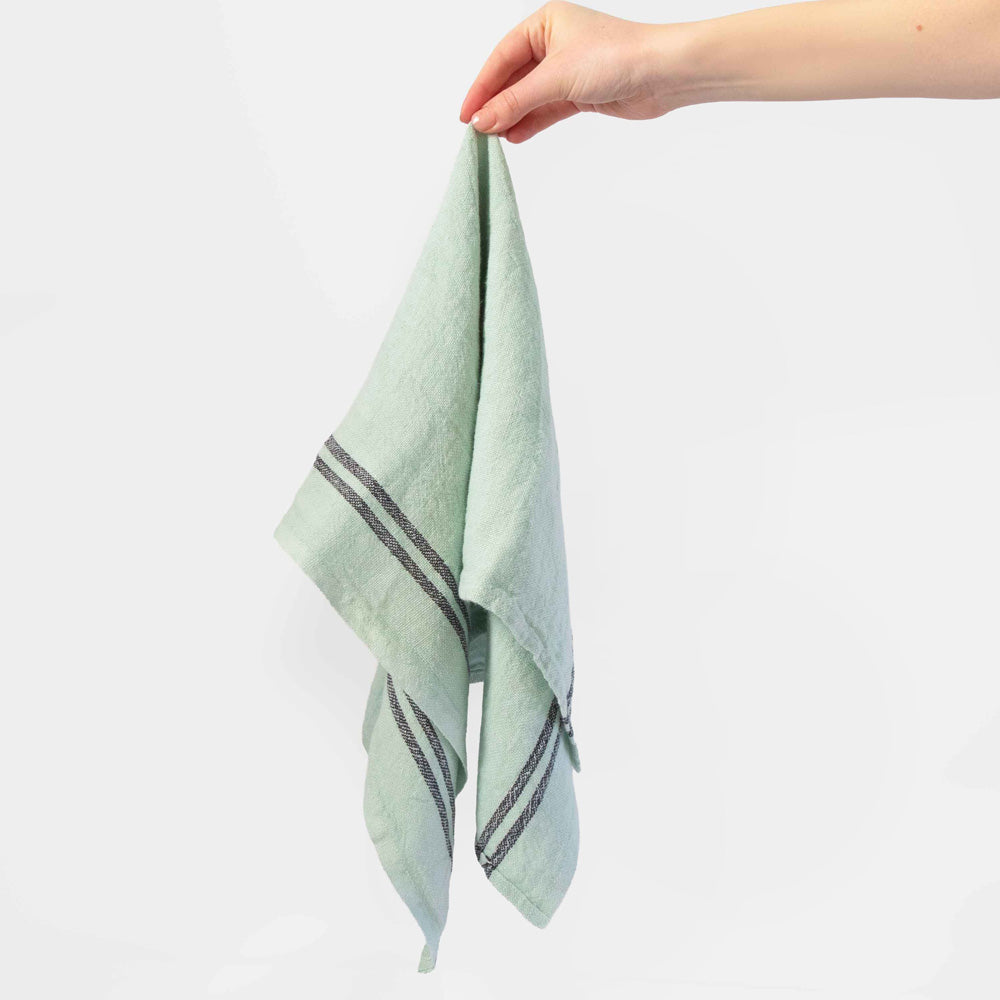 Hand holding a mint green tea towel with dark stripes on a white background