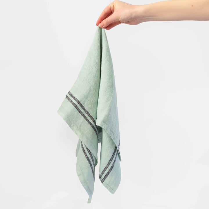 Hand holding a mint green tea towel with dark stripes on a white background