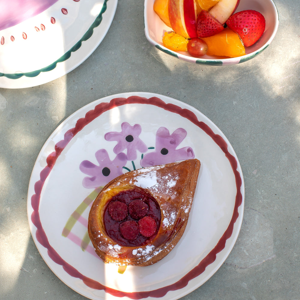 a tablescape featuring a pastry on a floral design ceramic plate and fruit in a heart shaped bowl 