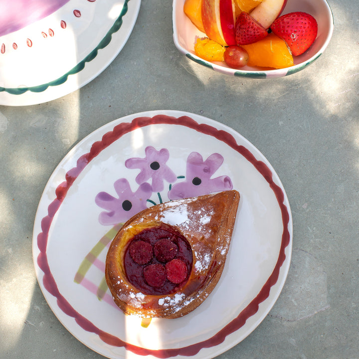 a tablescape featuring a pastry on a floral design ceramic plate and fruit in a heart shaped bowl 