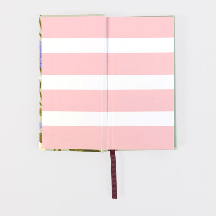 A hardcover notebook with alternating horizontal pink and white stripes on the cover, shown open with a burgundy ribbon bookmark against a light gray background.