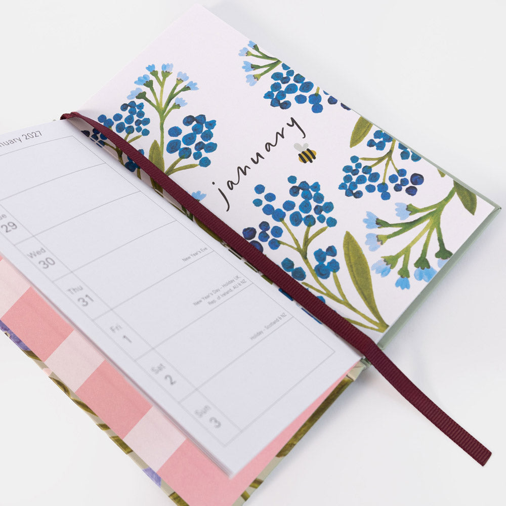 An open monthly planner with a floral cover design featuring blue forget-me-nots and green leaves on a white background. The cover is labeled 'January' with a small bee illustration.