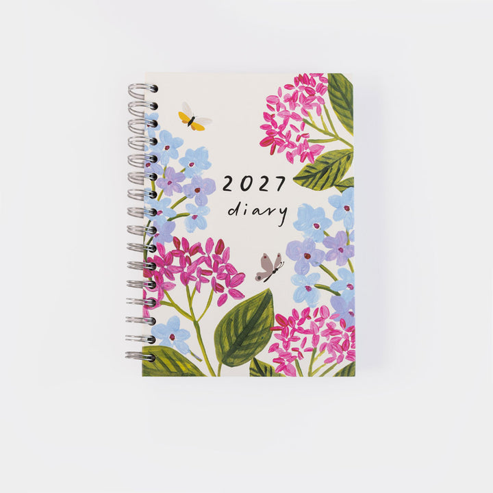 A spiral-bound 2027 diary featuring a watercolor floral cover design with pink and blue hydrangeas, green leaves, and small butterflies on a light background.