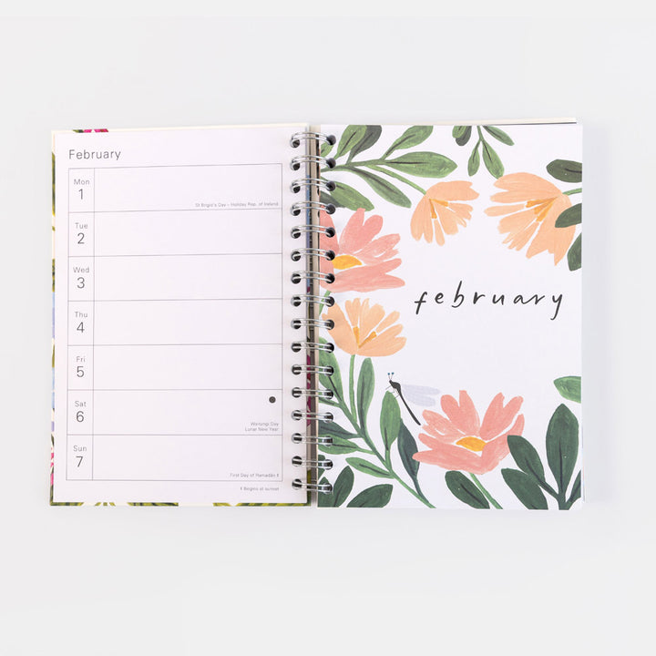 An open spiral-bound planner showing a February weekly layout on the left page and a floral cover design on the right page with peach flowers, green leaves, and the word 'February' in script.