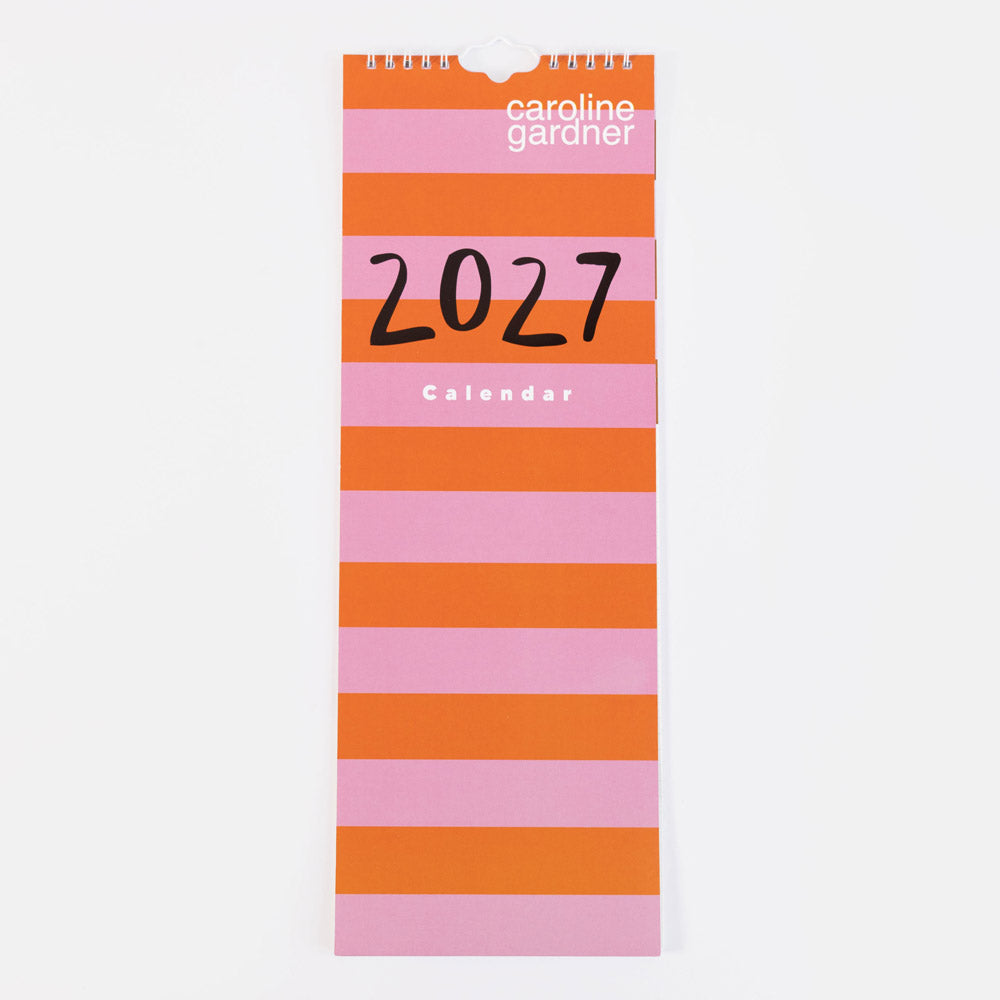A vertical 2027 wall calendar by Caroline Gardner with bold horizontal stripes in orange and pink, featuring black '2027' text and white brand text on a light gray background.