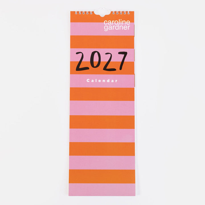 A vertical 2027 wall calendar by Caroline Gardner with bold horizontal stripes in orange and pink, featuring black '2027' text and white brand text on a light gray background.
