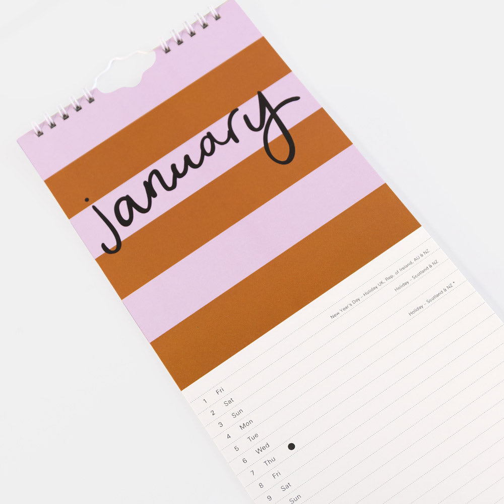 A spiral-bound monthly calendar page for January, shown diagonally on a white background. The cover features alternating horizontal stripes in light pink and terracotta brown with the word 'January' written in black script across the top.