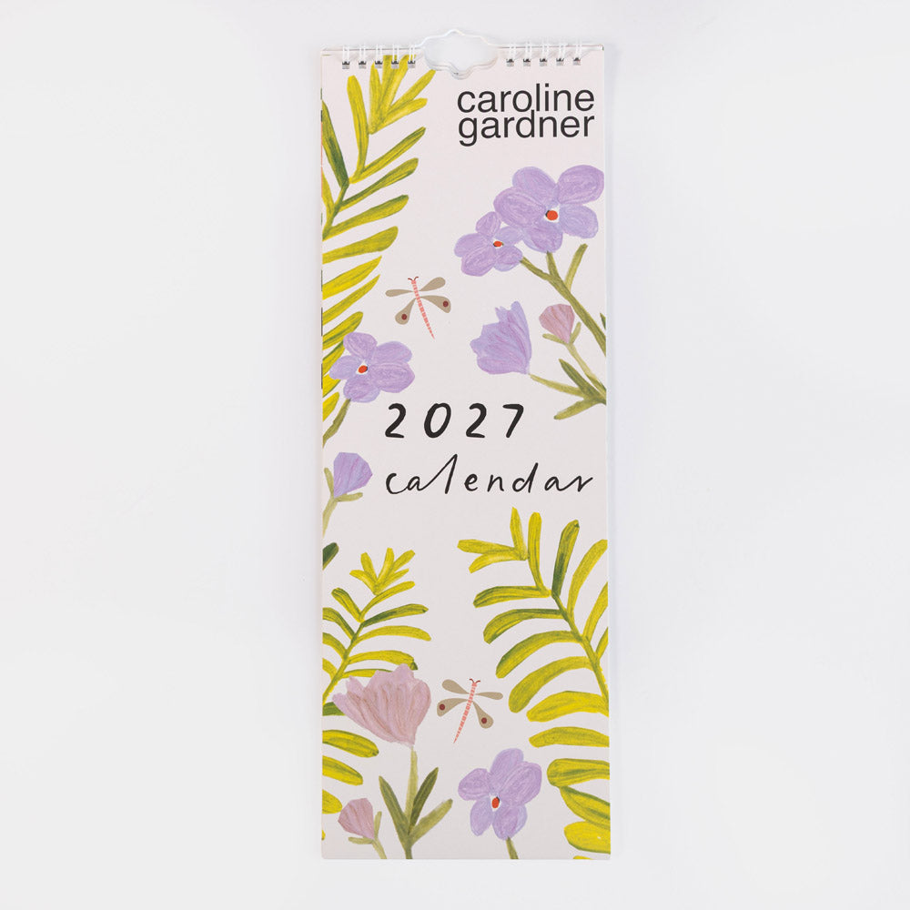 Caroline Gardner 2027 wall calendar featuring a botanical cover design with purple flowers, green and yellow leaves, and dragonflies on a white background.