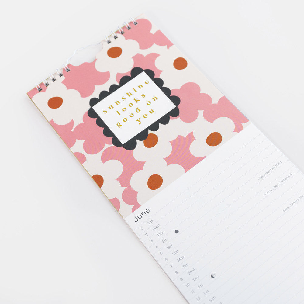 A spiral-bound calendar with a pink and white floral patterned cover, featuring a central label that reads 'sunny side up' and showing the month of June on a white lined page.