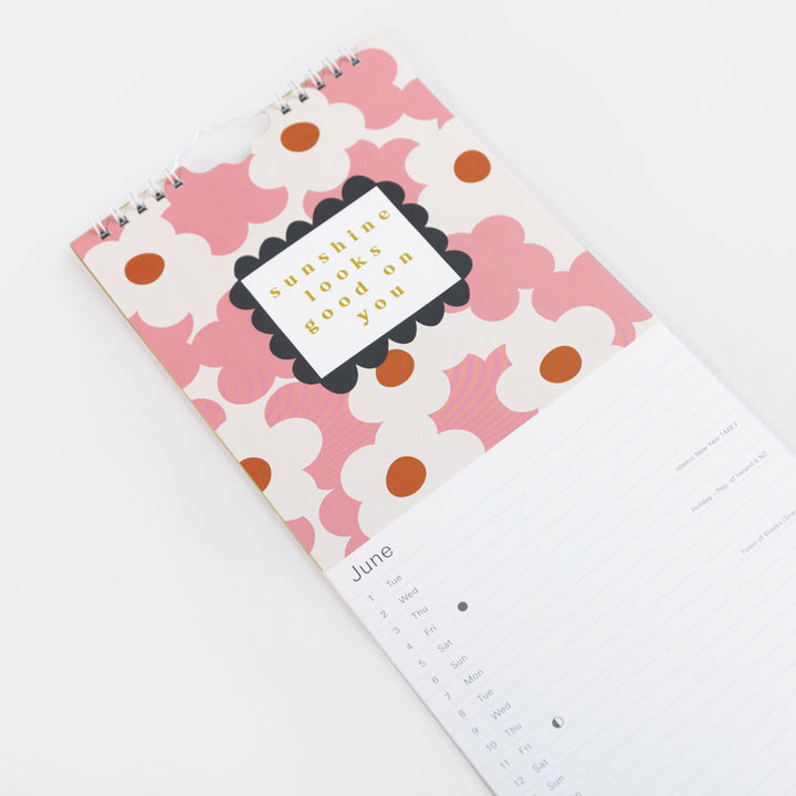 A spiral-bound calendar with a pink and white floral patterned cover, featuring a central label that reads 'sunny side up' and showing the month of June on a white lined page.