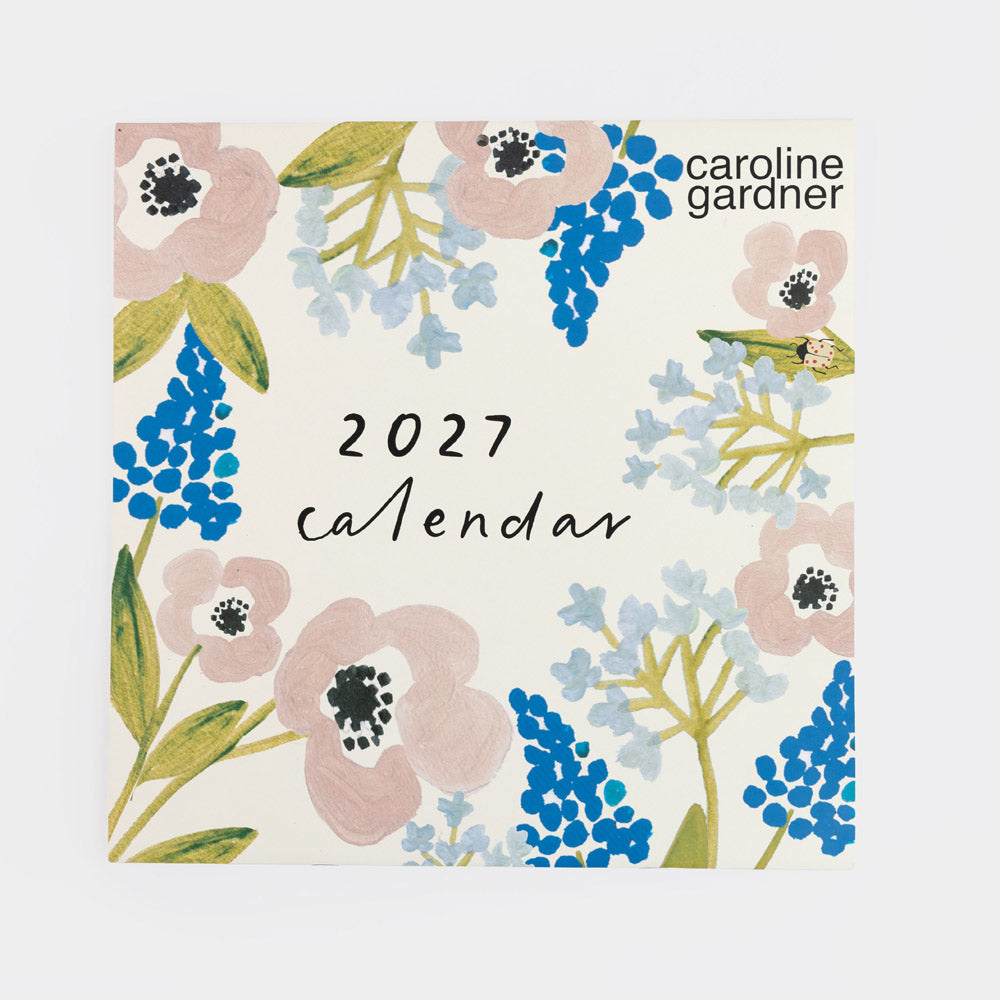 A square 2027 Caroline Gardner calendar with a floral border design in pink, blue, green, and light blue on an off-white background.