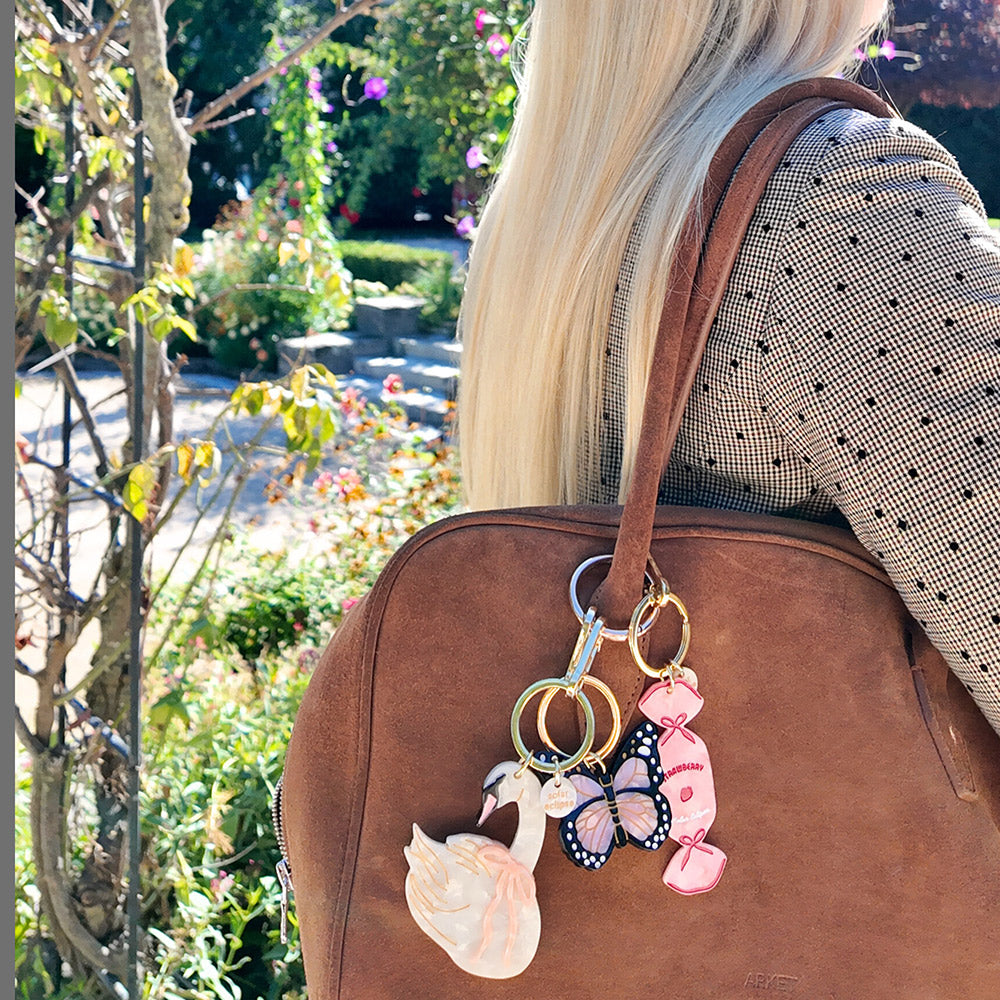 Brown leather bag with decorative bag charms featuring a swan, butterfly, and sweet