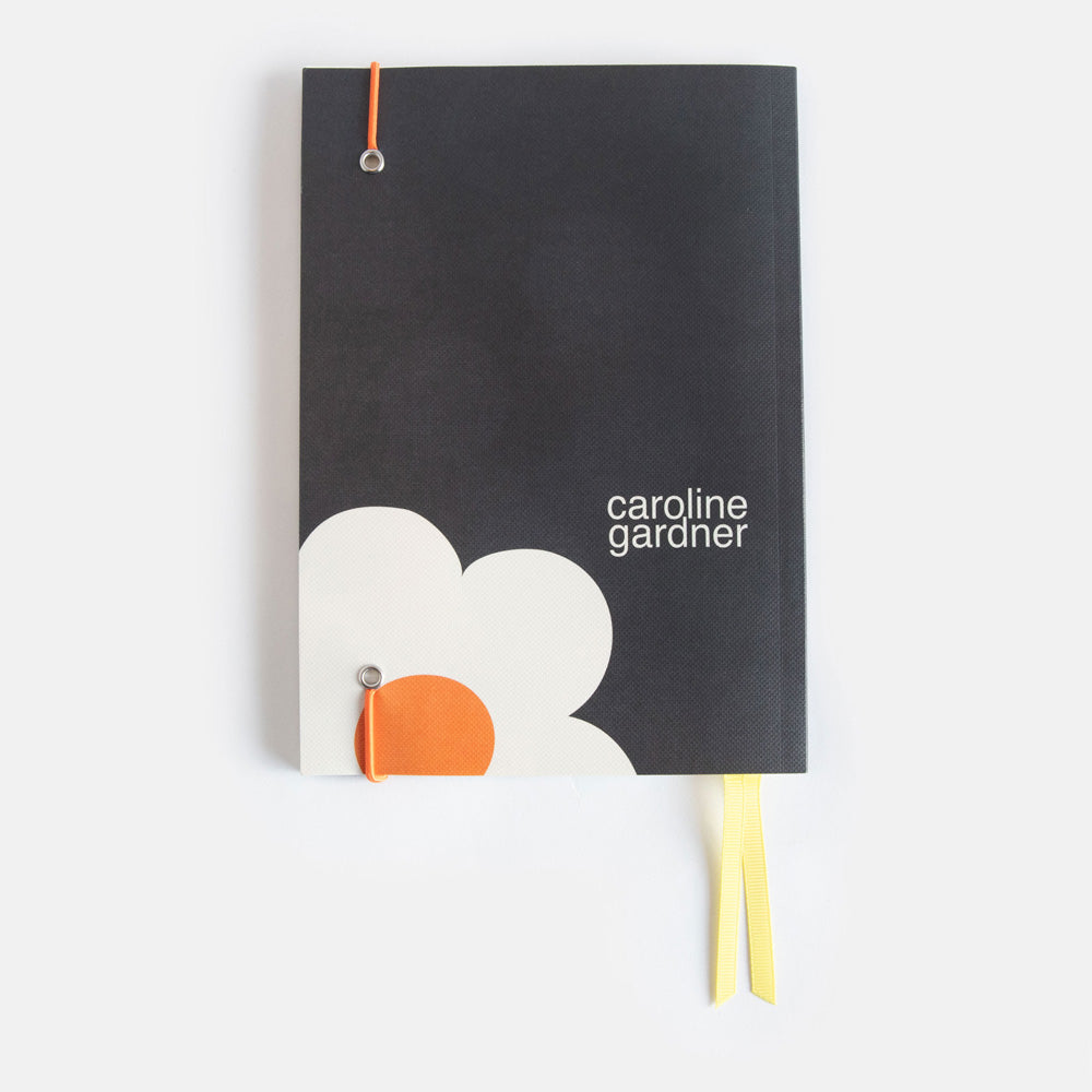 A5 softback notebook with a big cream flower on a charcoal background design, yellow ribbon page markers and orange elastic band