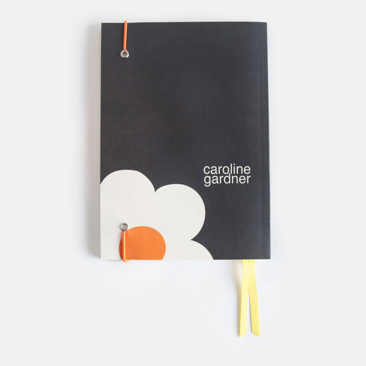 A5 softback notebook with a big cream flower on a charcoal background design, yellow ribbon page markers and orange elastic band